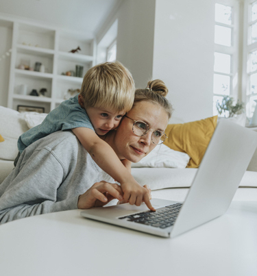 Boy looking over mum's shoulder at laptop screen