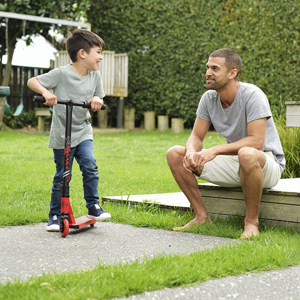 Boy on scooter in garden with dad