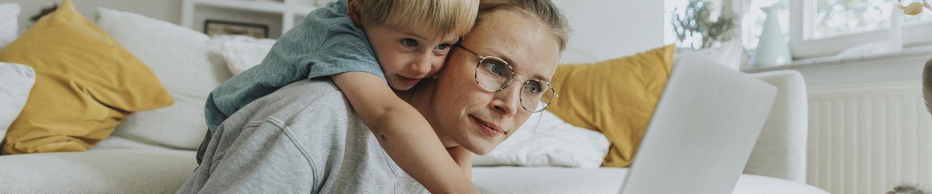 Boy looking over mum's shoulder at laptop screen